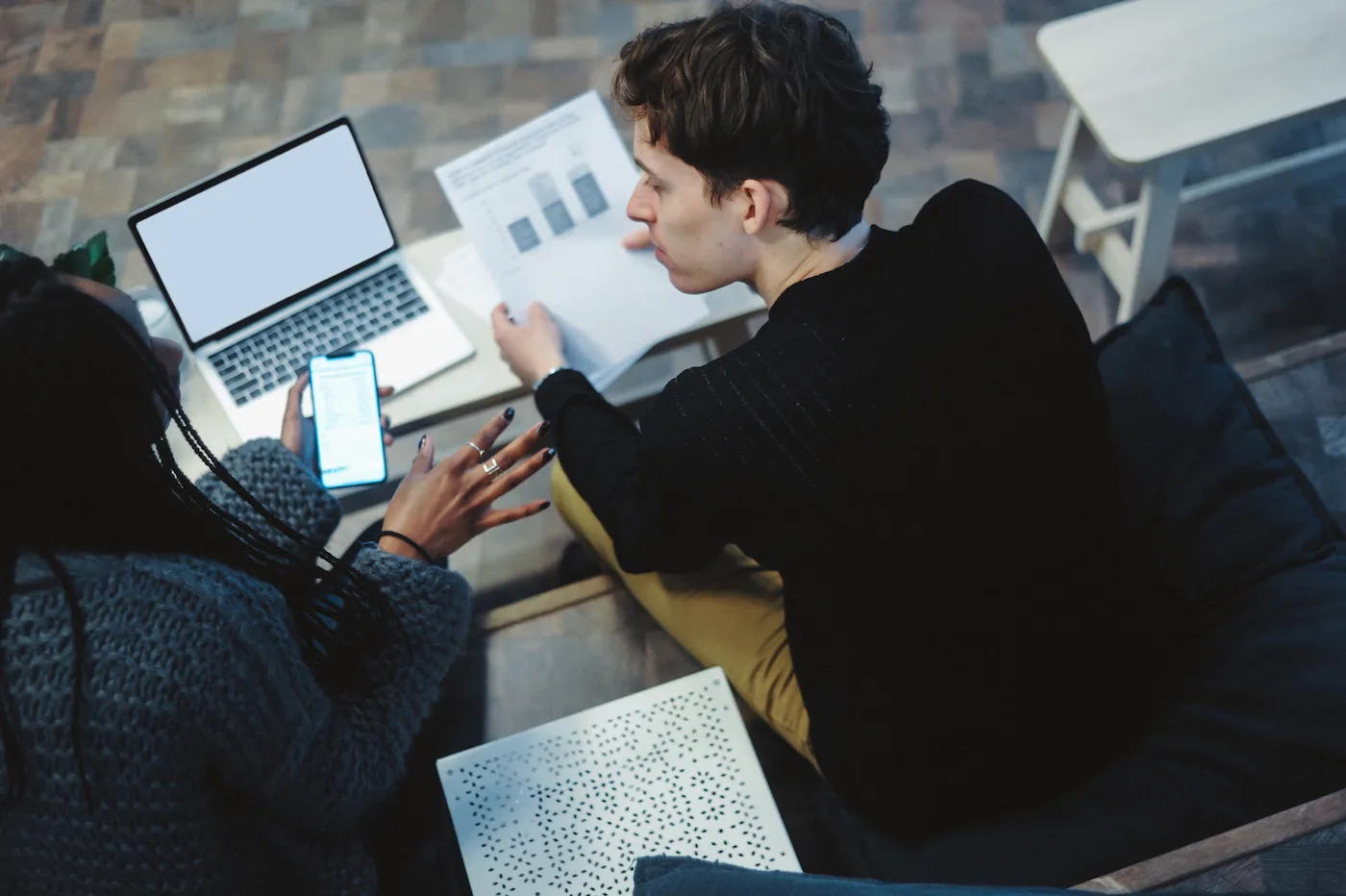 Two people sitting and discussing finances with papers, asmartphone and a laptop