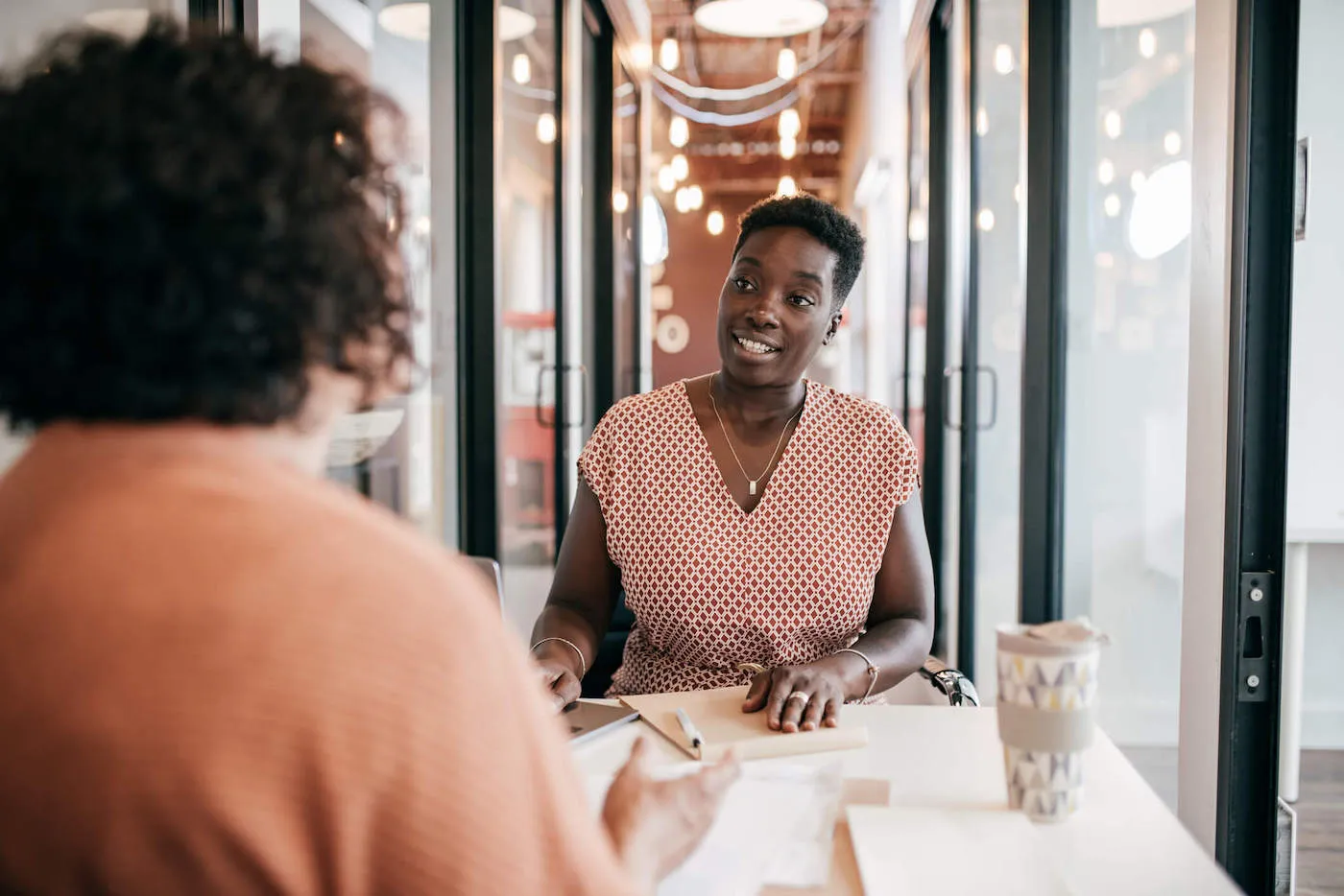 Two seated women conversing in open office space.