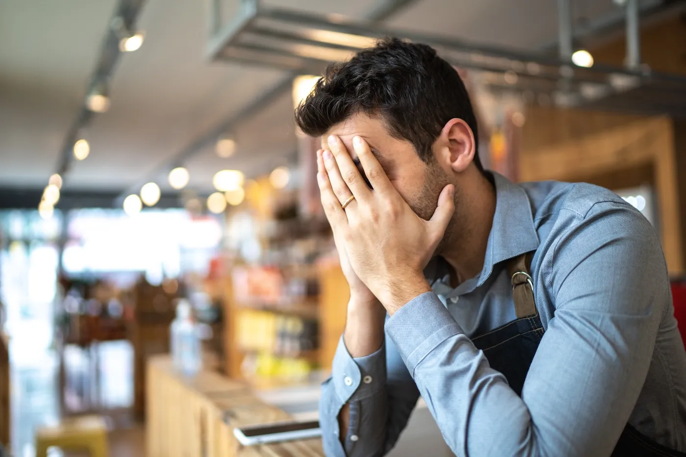 A stressed man going through bankruptcy. He is holding his face in his hands.