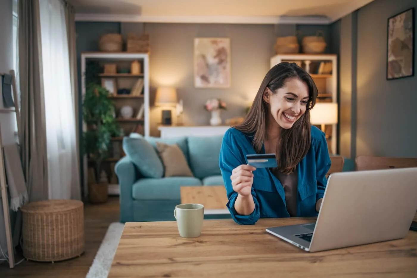 Young woman checking her credit score on her laptop while holding a credit card and having a coffee