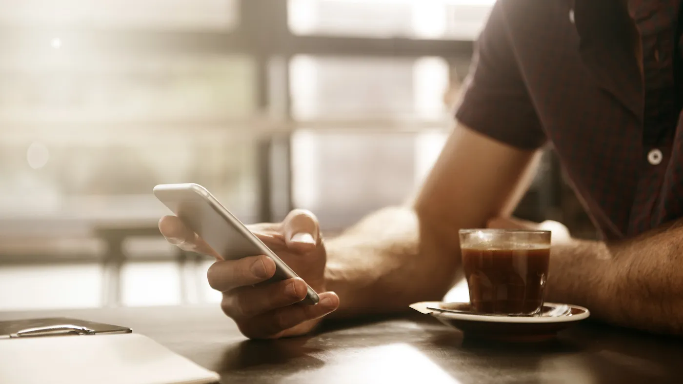 Cropped shot of a man using cellphone at a cafe to open a high-yield savings account online.