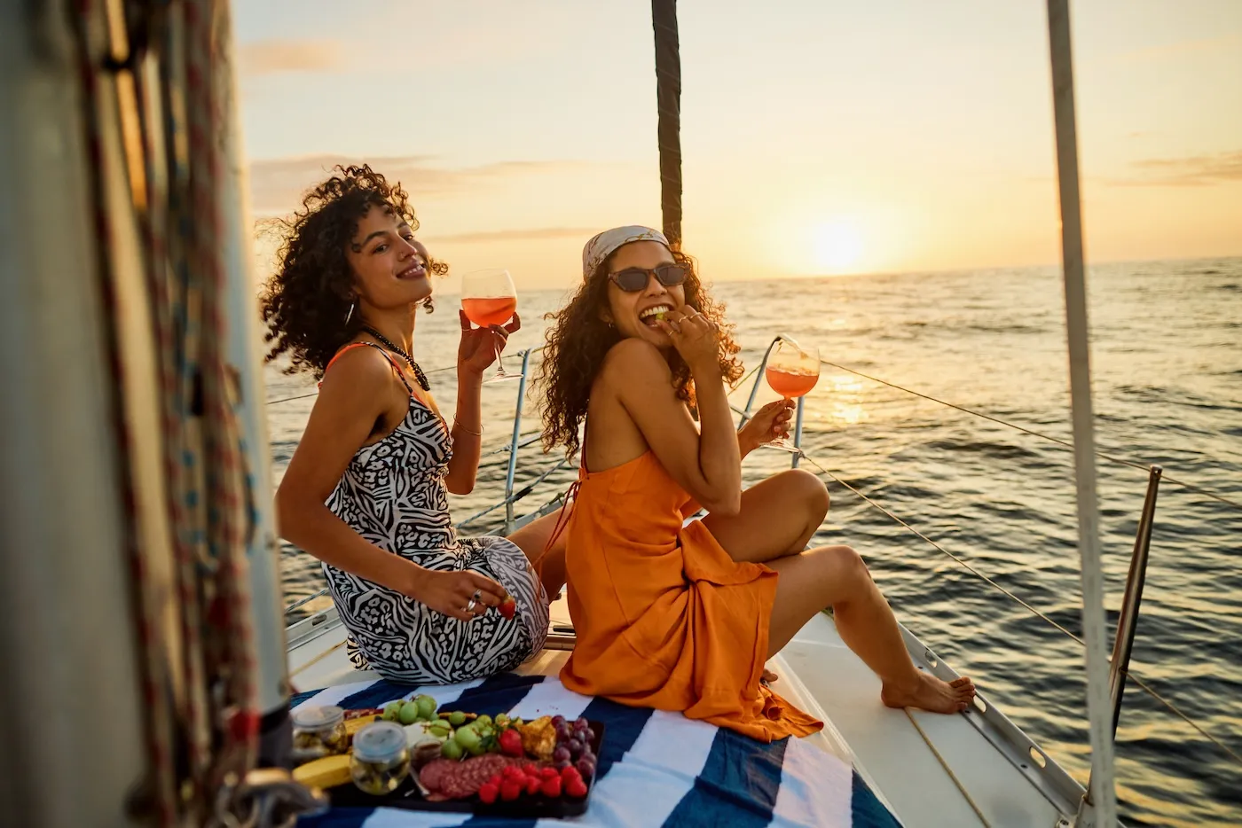 Young stylish female friends enjoying a charcuterie plate onboard a luxury sailing yacht during golden hour.