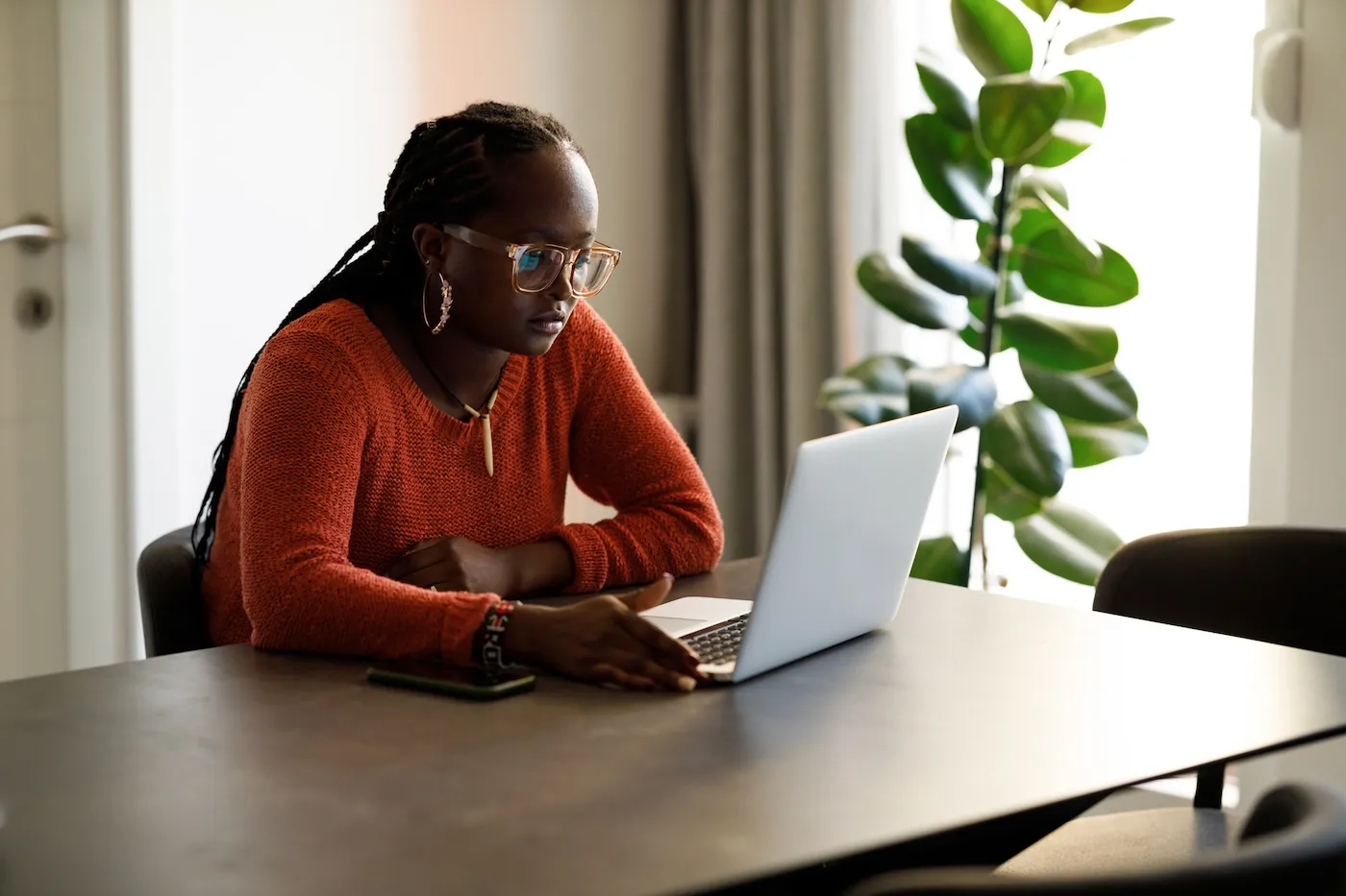 A young woman is sitting comfortably while working on finances from her sunny living room.