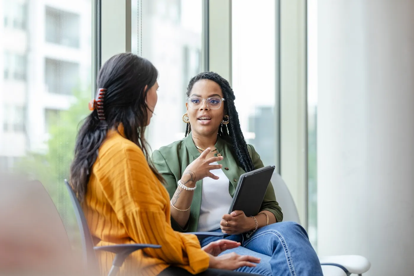 Two women speaking to each other near a window in an office.