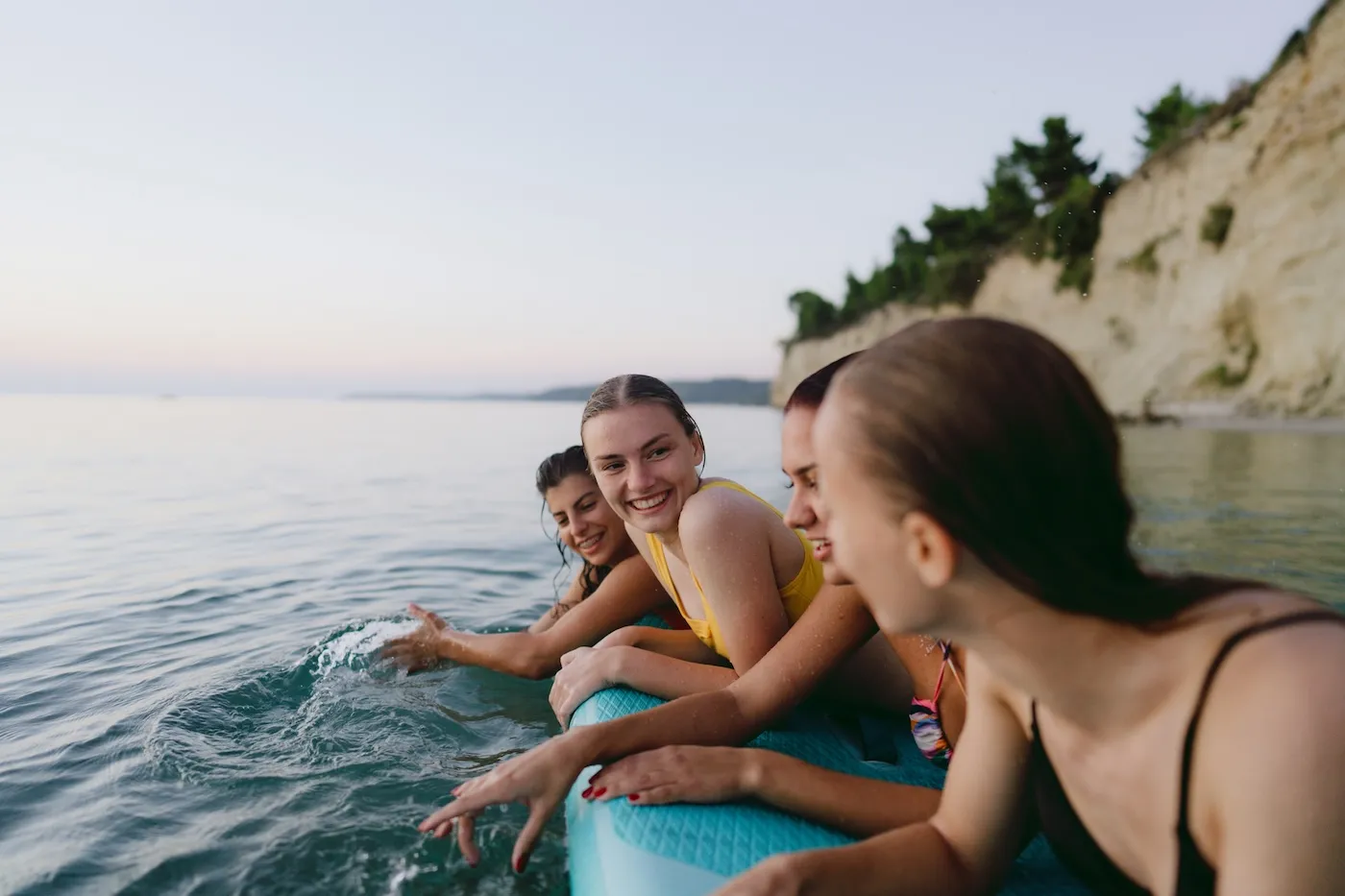 Photo of young women in the sea at sunset, holding onto a paddle board.