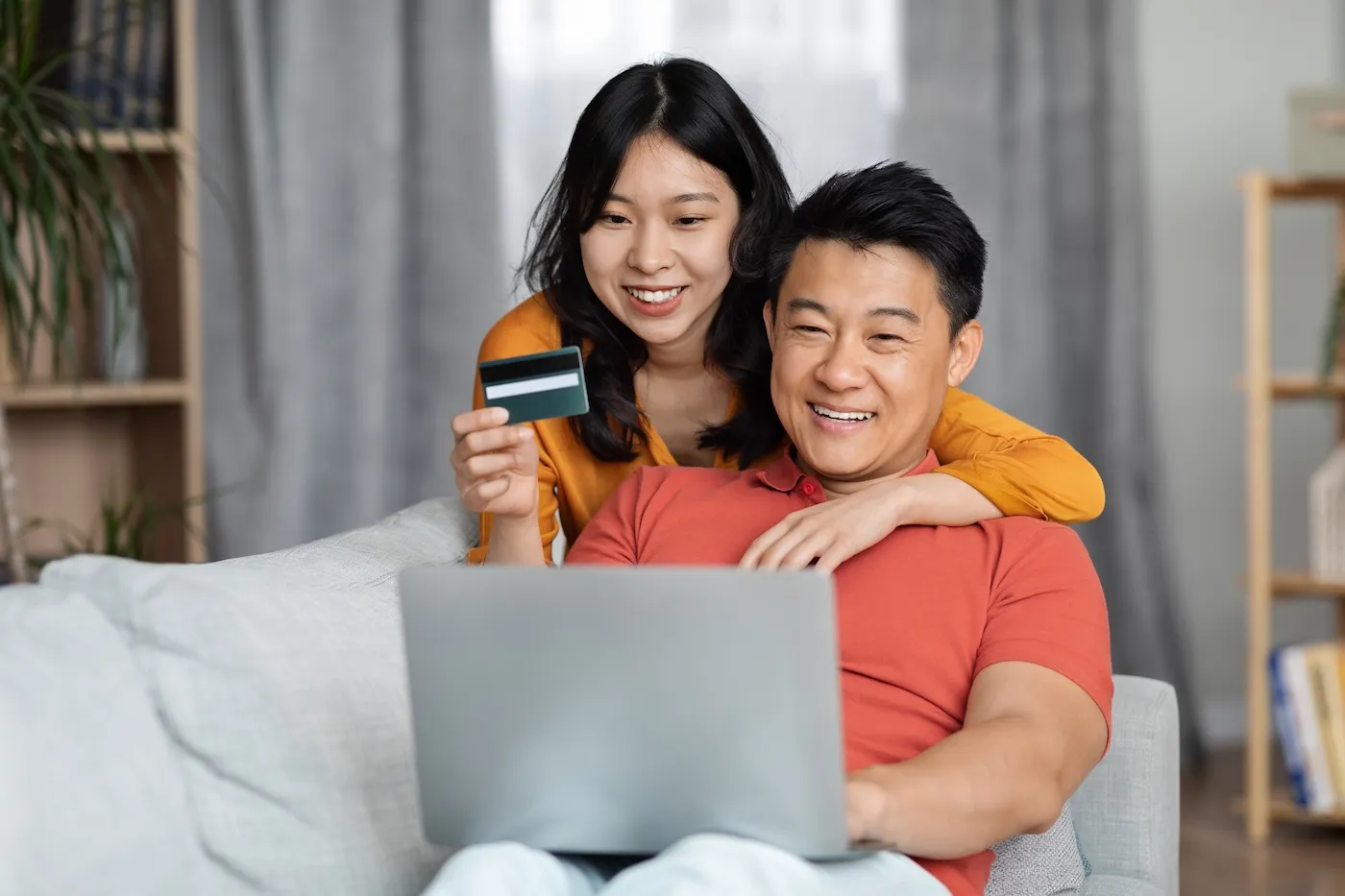 Happy husband and wife embracing, using laptop computer and plastic credit card.