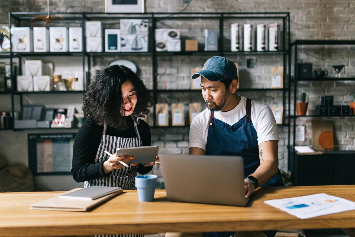 Two small business owners work behind cafe counter. The owners of the coffee shop engage in discussion about finances for the business.