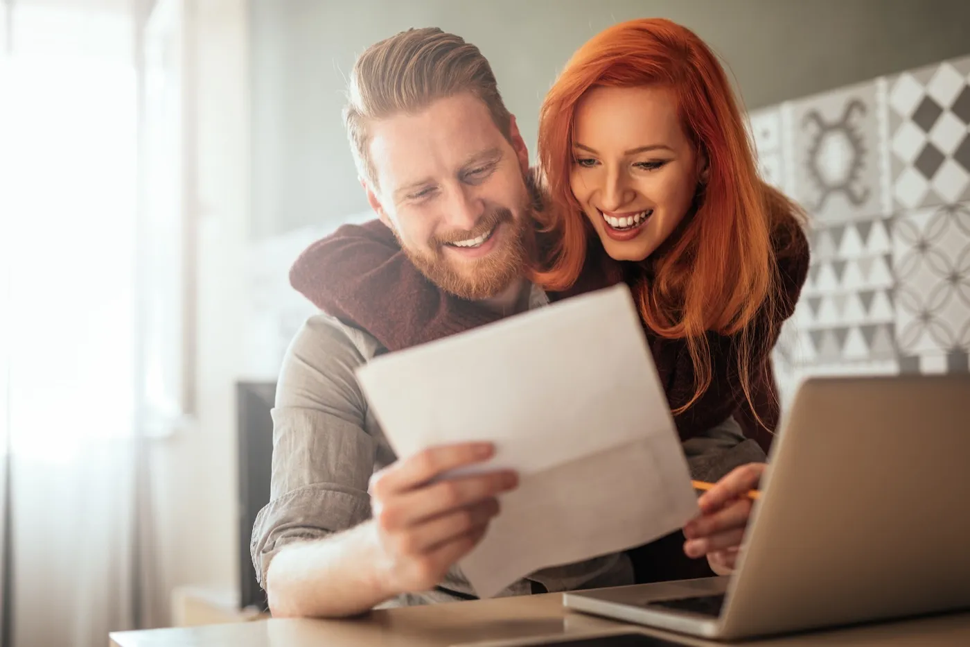 Photo of a positive young couple embracing and looking at checking statements at home.