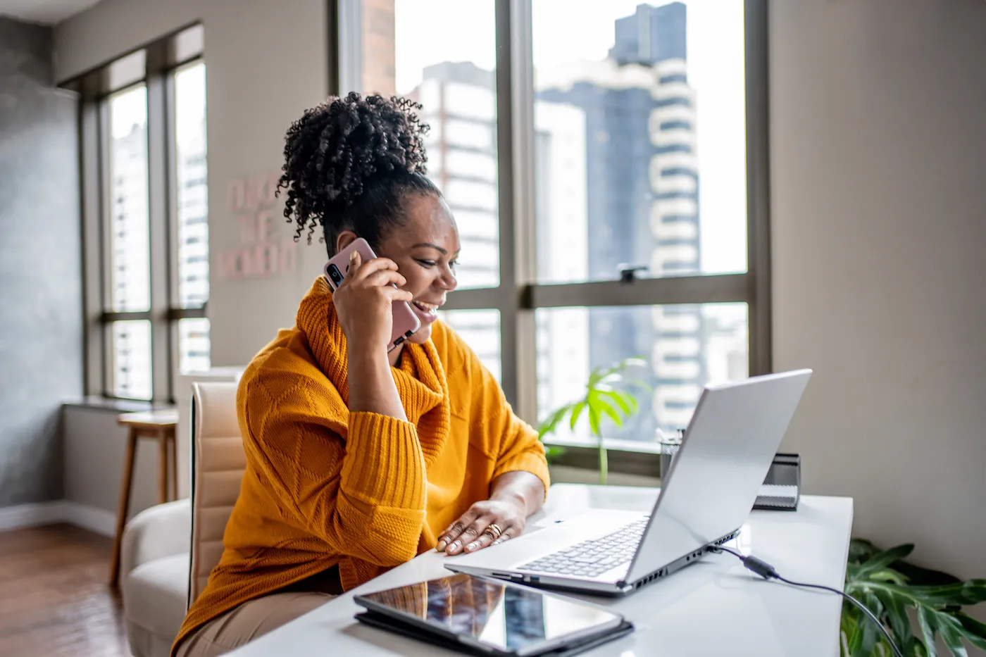 A happy woman who has just received a financial windfall is talking on the phone while looking at her laptop