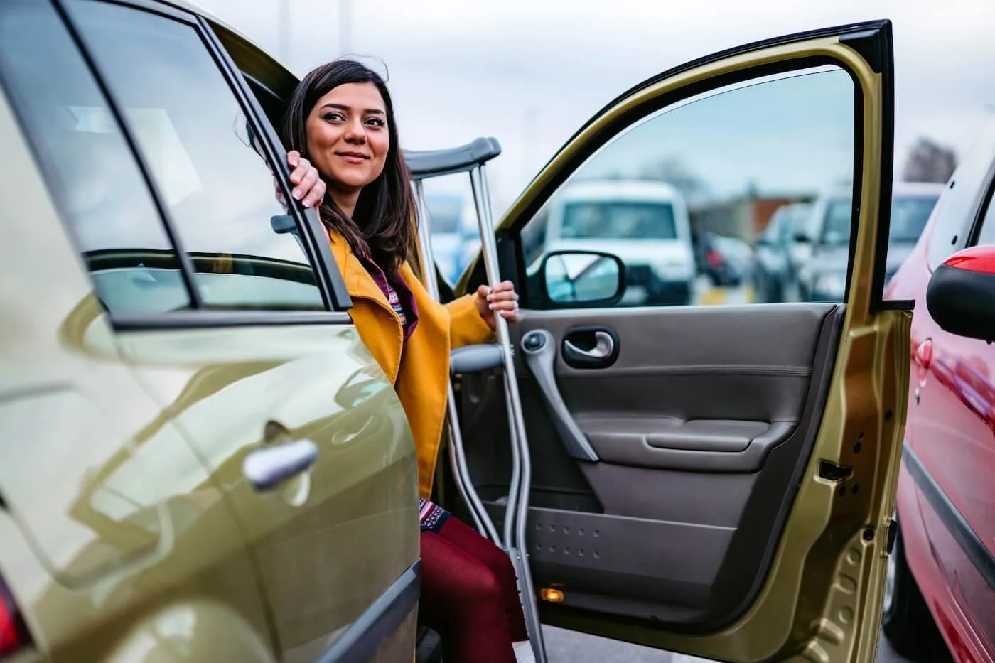 Smiling woman using crutches while stepping out of a car in a parking lot.