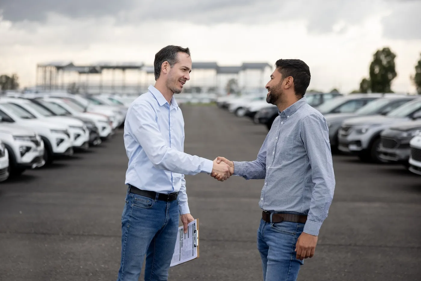 Happy salesman handshaking with a client after buying a car at the dealership.