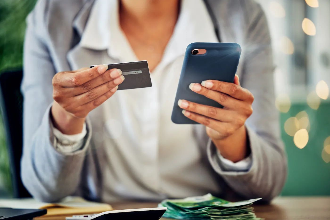 A person sitting at a table, holding a mobile phone in one hand and a credit card in the other.