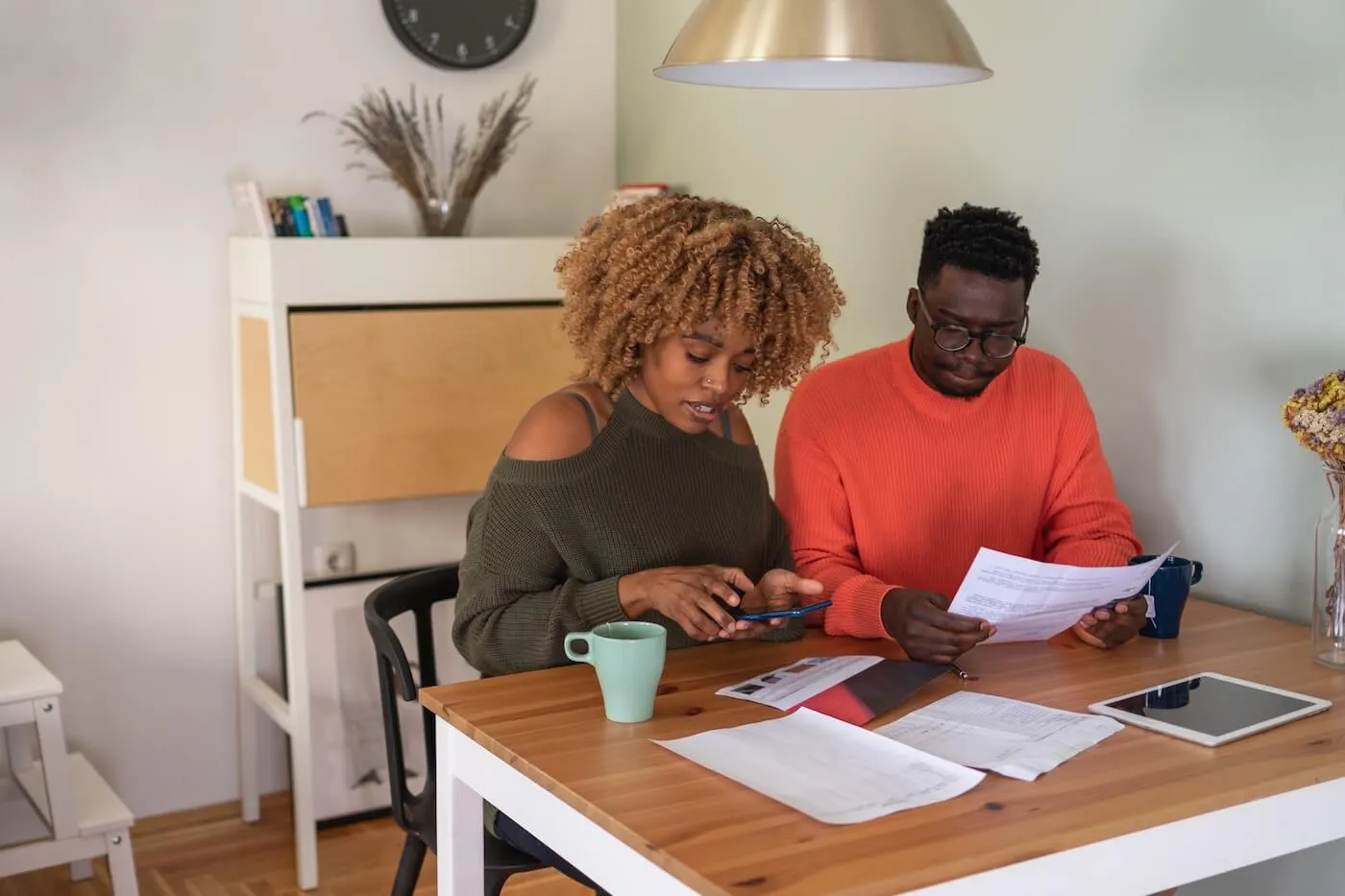 Focused couple reviewing their bills at home, with a coffee mug and a tablet on the desk