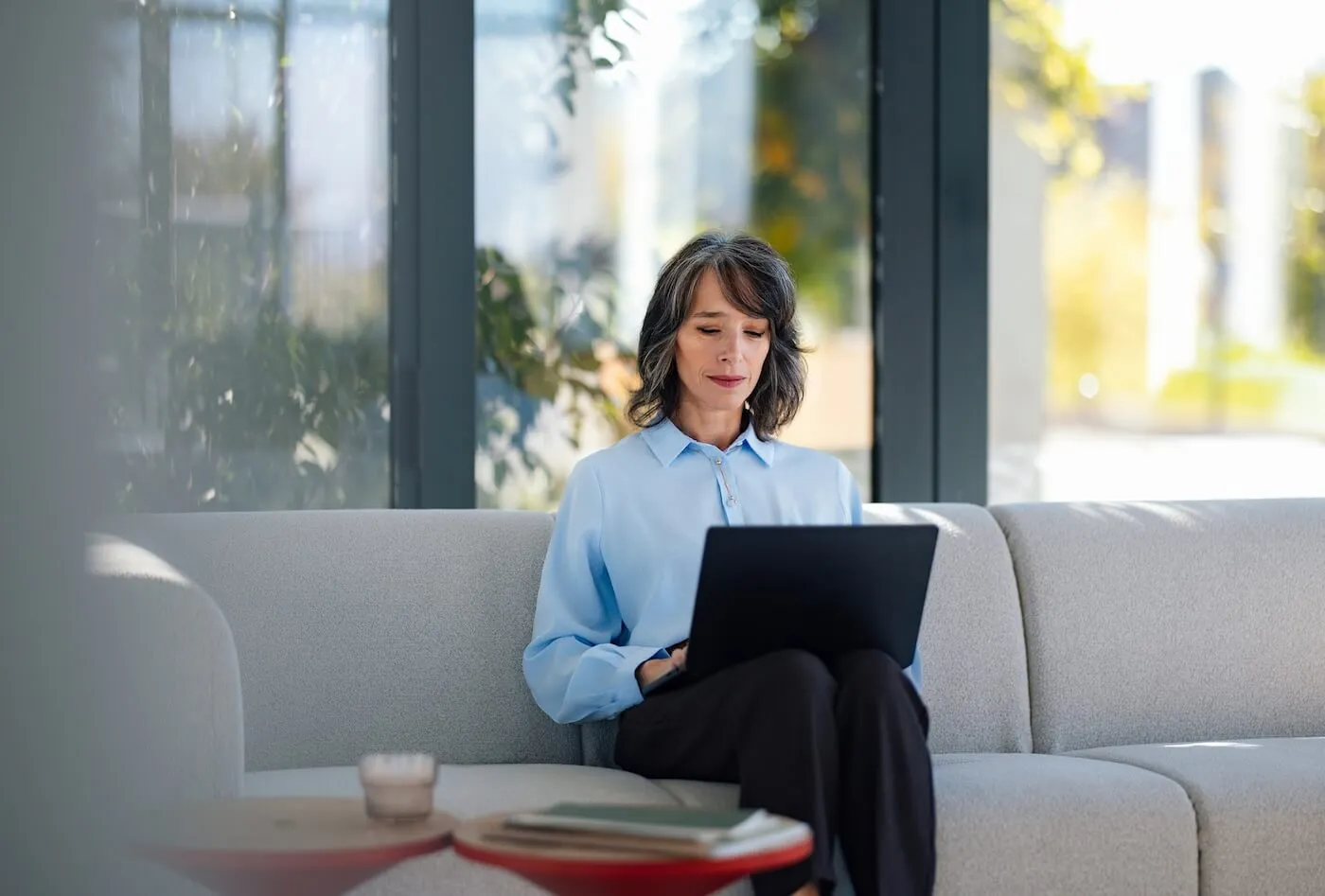 Focused mature woman using her laptop while sitting on a sofa with the small side tables