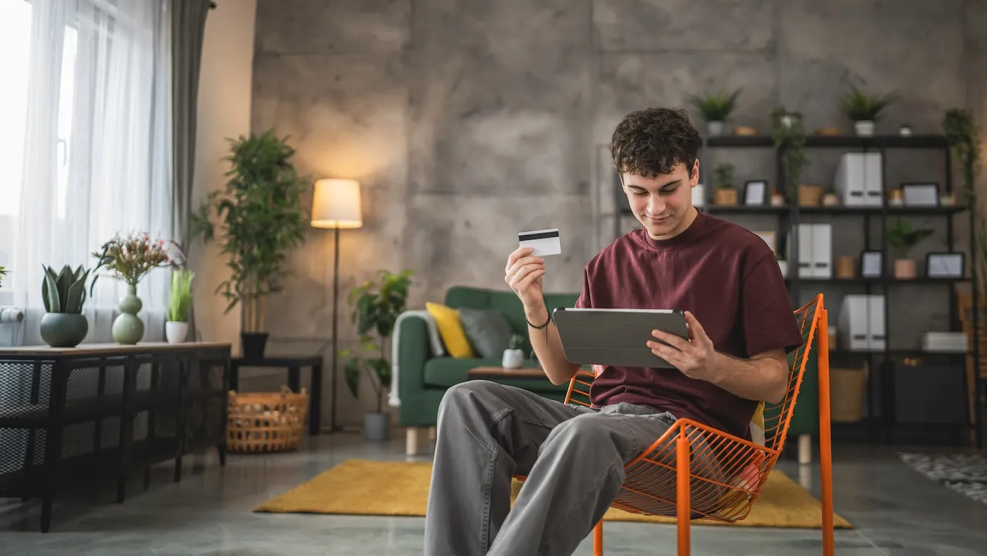 A teenage young man sits at home using a credit card for shopping online