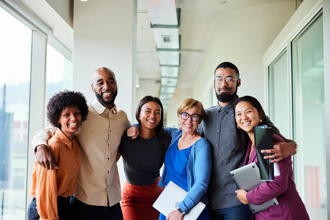 Portrait of a group of diverse businesspeople smiling while standing arm in arm together in an office corridor