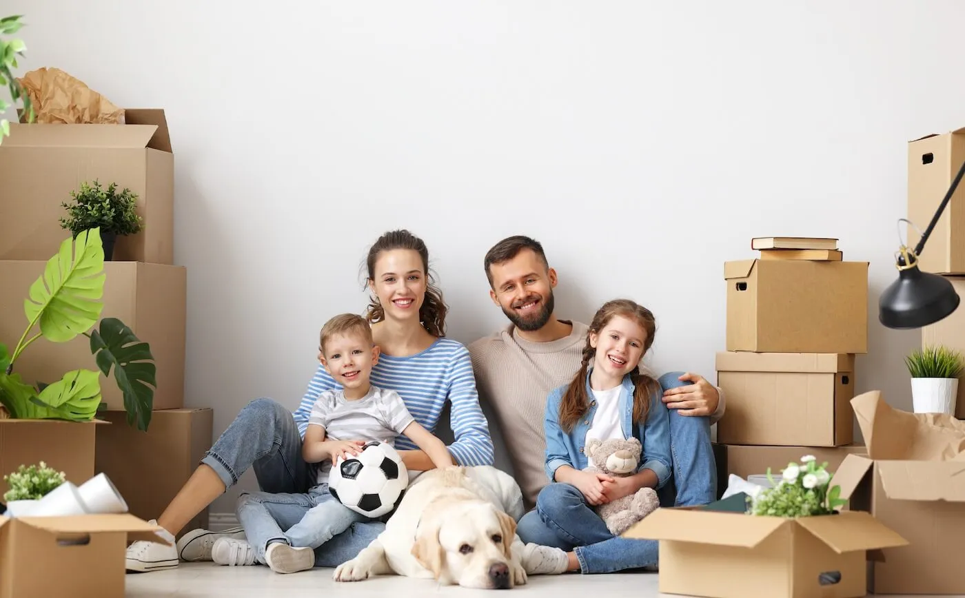 Family of 4 with a dog sitting on the floor of their new house surrounded by boxes