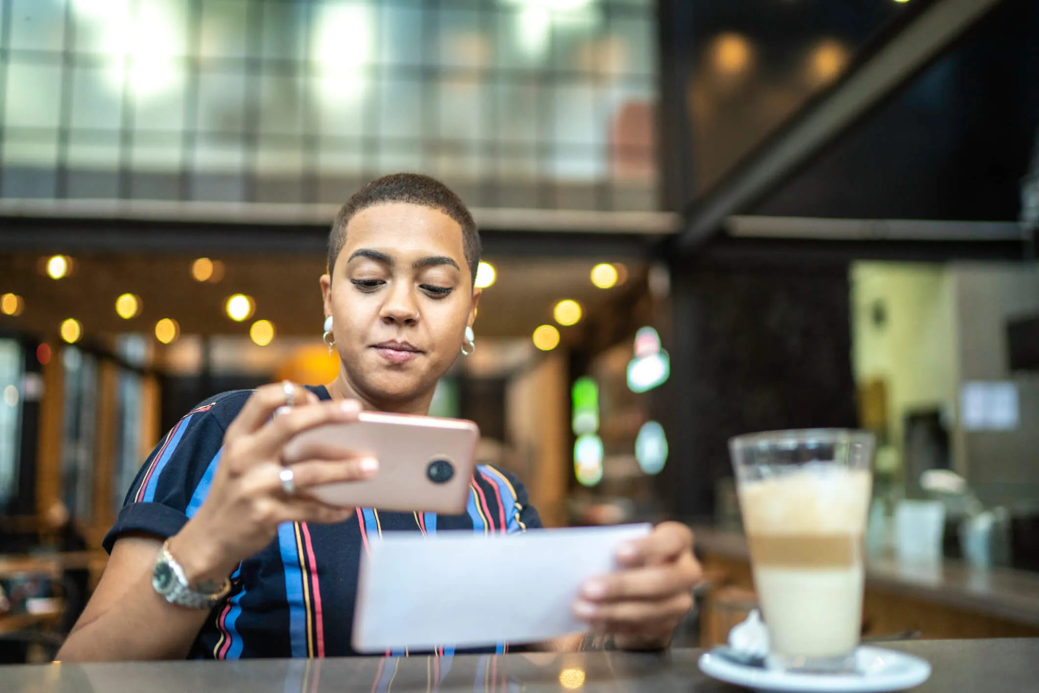 Woman taking a photo of a check to make a mobile check deposit while having coffee