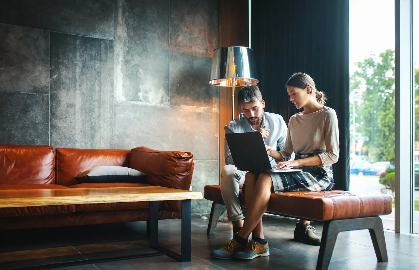 Closeup side view of couple of mid 20's couple sitting on a sofa and using laptops to assess their net worth.