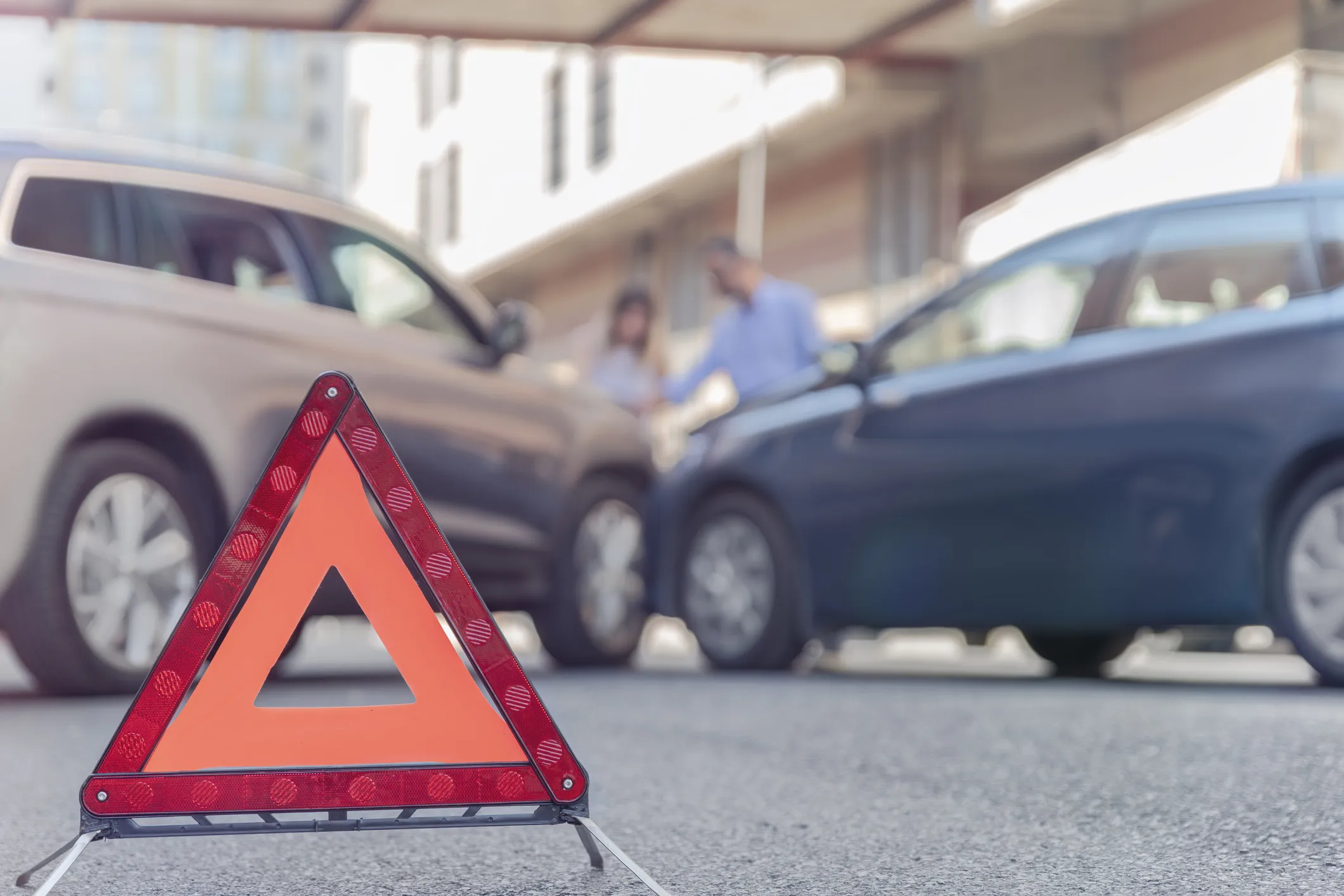 Two cars that have crashed into each other at an angle with a hazard sign on the road.