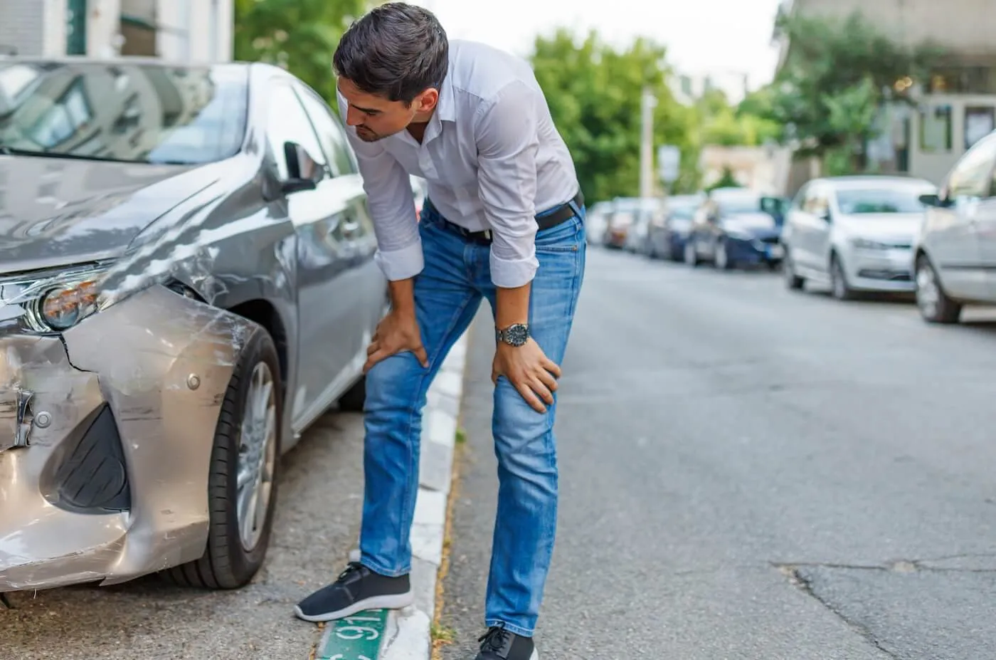 Man standing on a street beside a damaged car, assessing the damage.