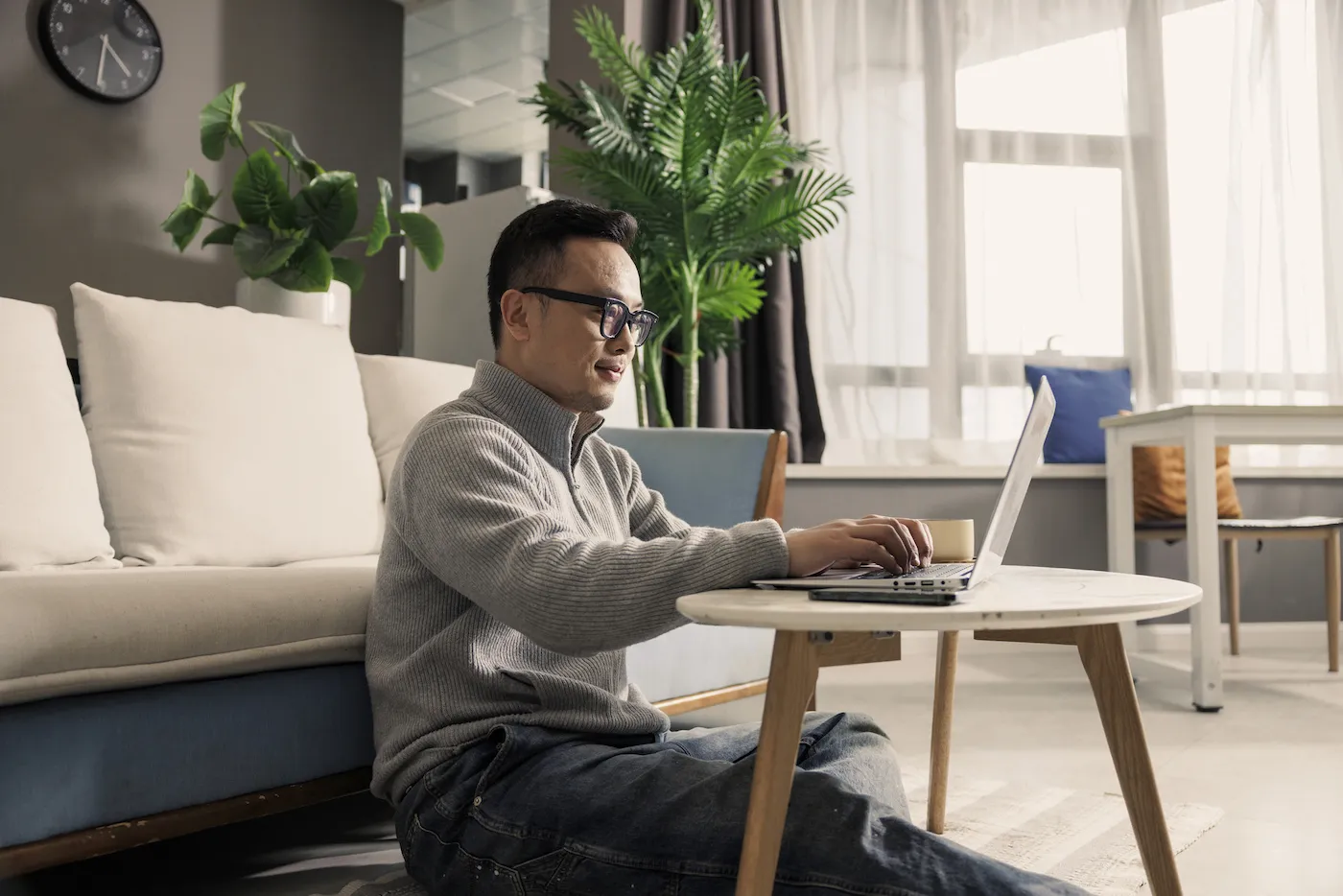 A man sitting on the floor in front of a couch working on his laptop on a small table.