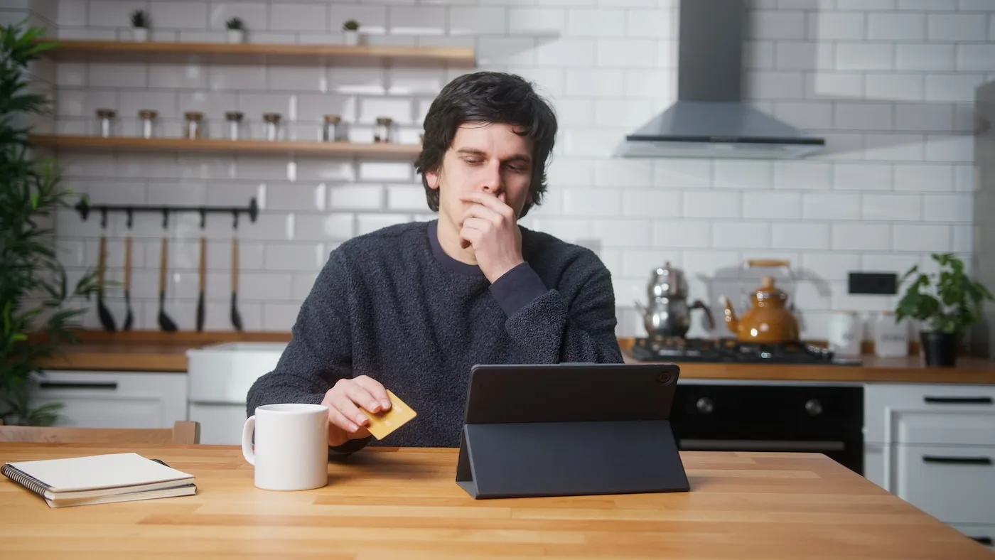 A man sitting in kitchen at home entering credit card number on tablet device. Credit card is declined or out of limit.