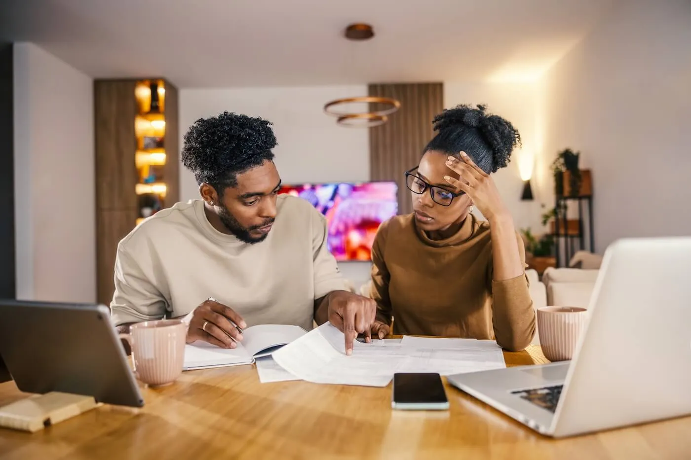 Focused young couple filing taxes at home, with a laptop, a smartphone, and printed documents on a desk