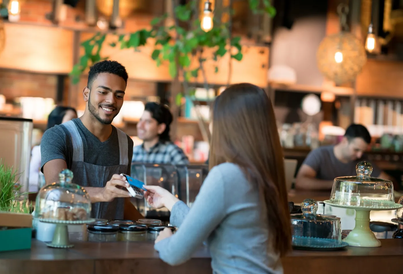 Happy woman making a contactless payment at a restaurant with a credit card.