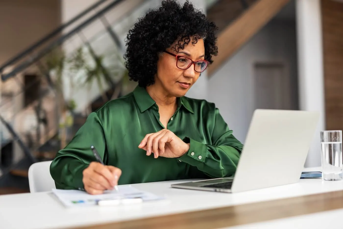 Focused businesswoman using her laptop in the office while making notes
