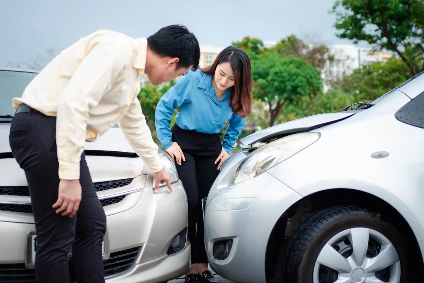 Two office workers, male and female, inspecting their cars after a minor accident on a parking lot