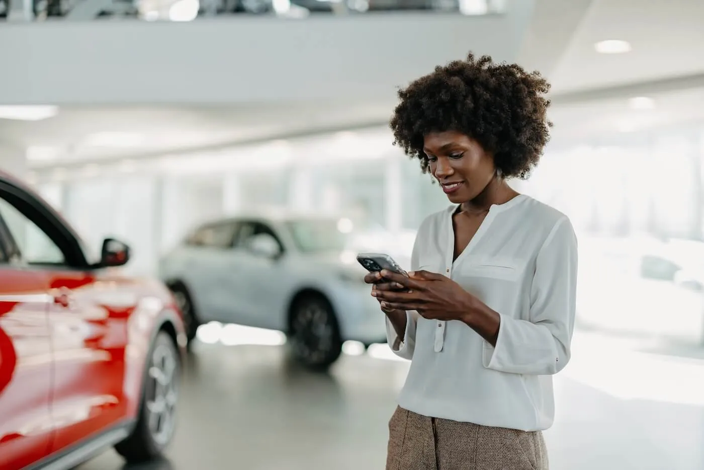 Smiling woman checking the current auto loan rates on her smartphone in the dealership showroom