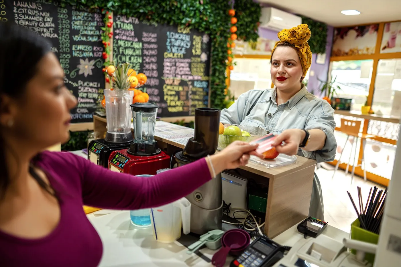 A woman paying for her meal at a colorful cafe with a debit card, handing it to the cashier.