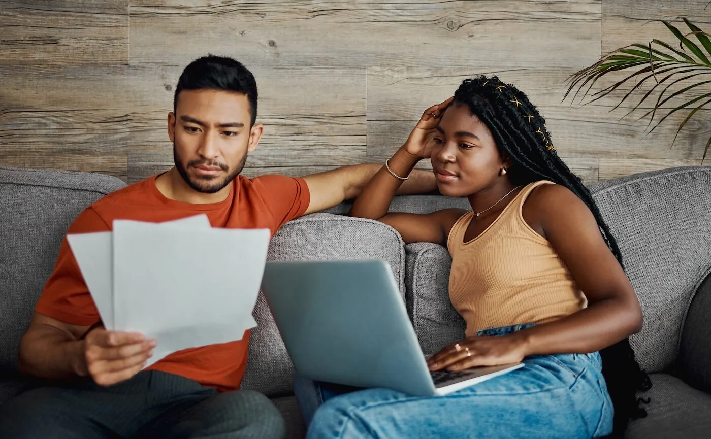 Couple using a laptop while reviewing paperwork in the living room