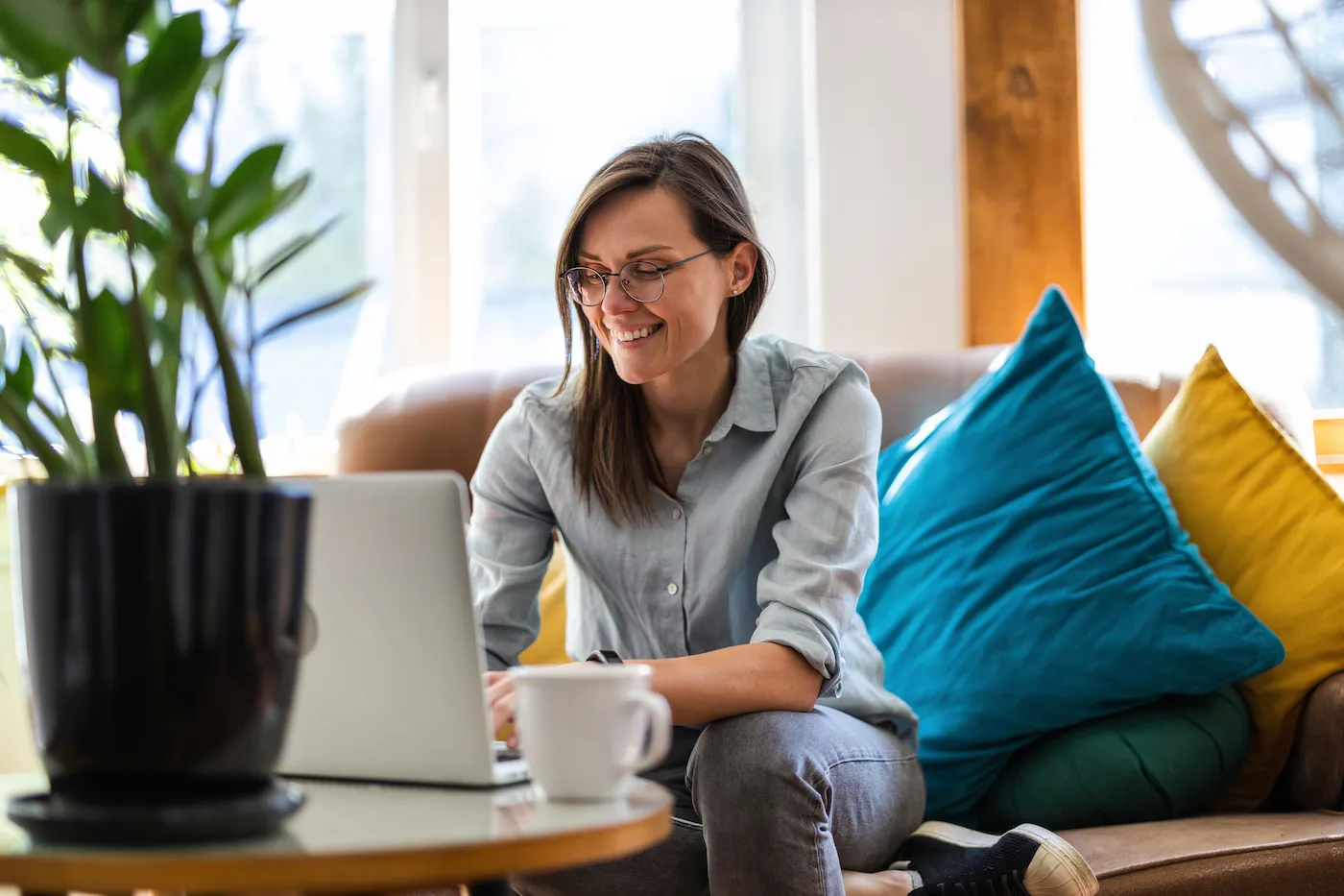 Young woman sitting on her couch using a laptop to budget for fixed and variable expenses.