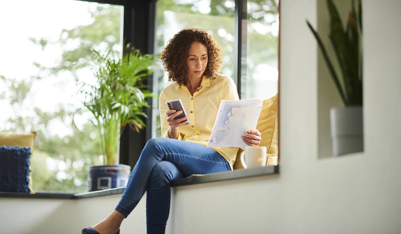 Woman budgeting on her phone with an app and papers