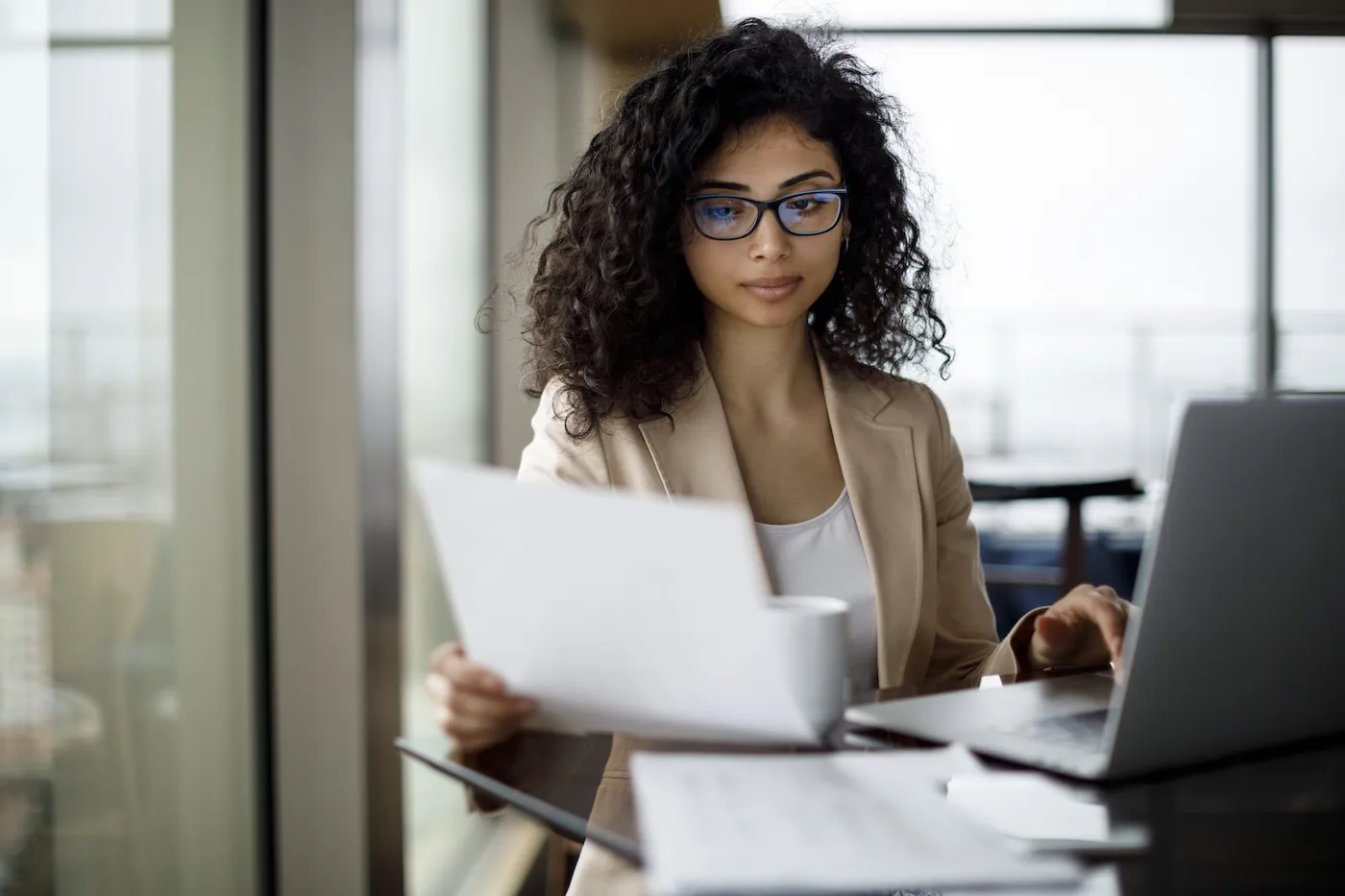 Woman creating debt management plan, sitting in front of a laptop and papers at a desk in an office.