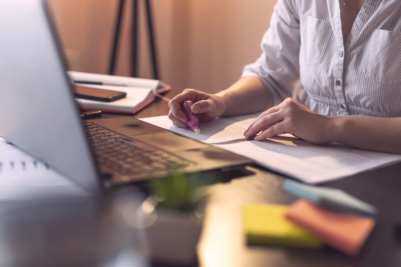 Detail of woman's hands correcting mistakes with an ink corrector, sitting in front of a laptop at a desk.