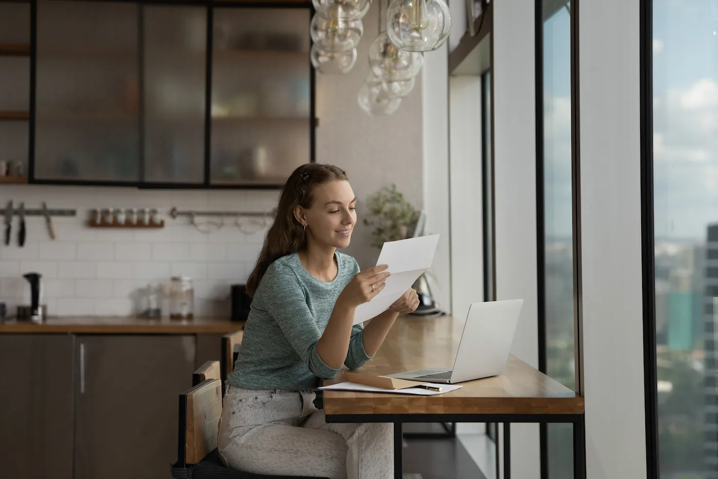 Happy young woman reading positive bank statement at home workplace with laptop.