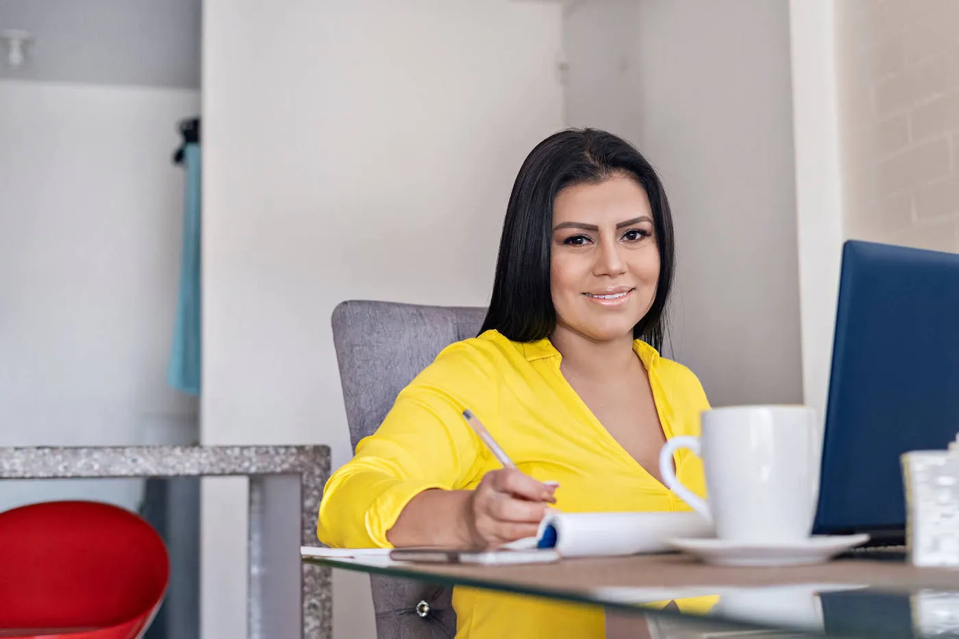 Woman in yellow shirt seated by desk writing.