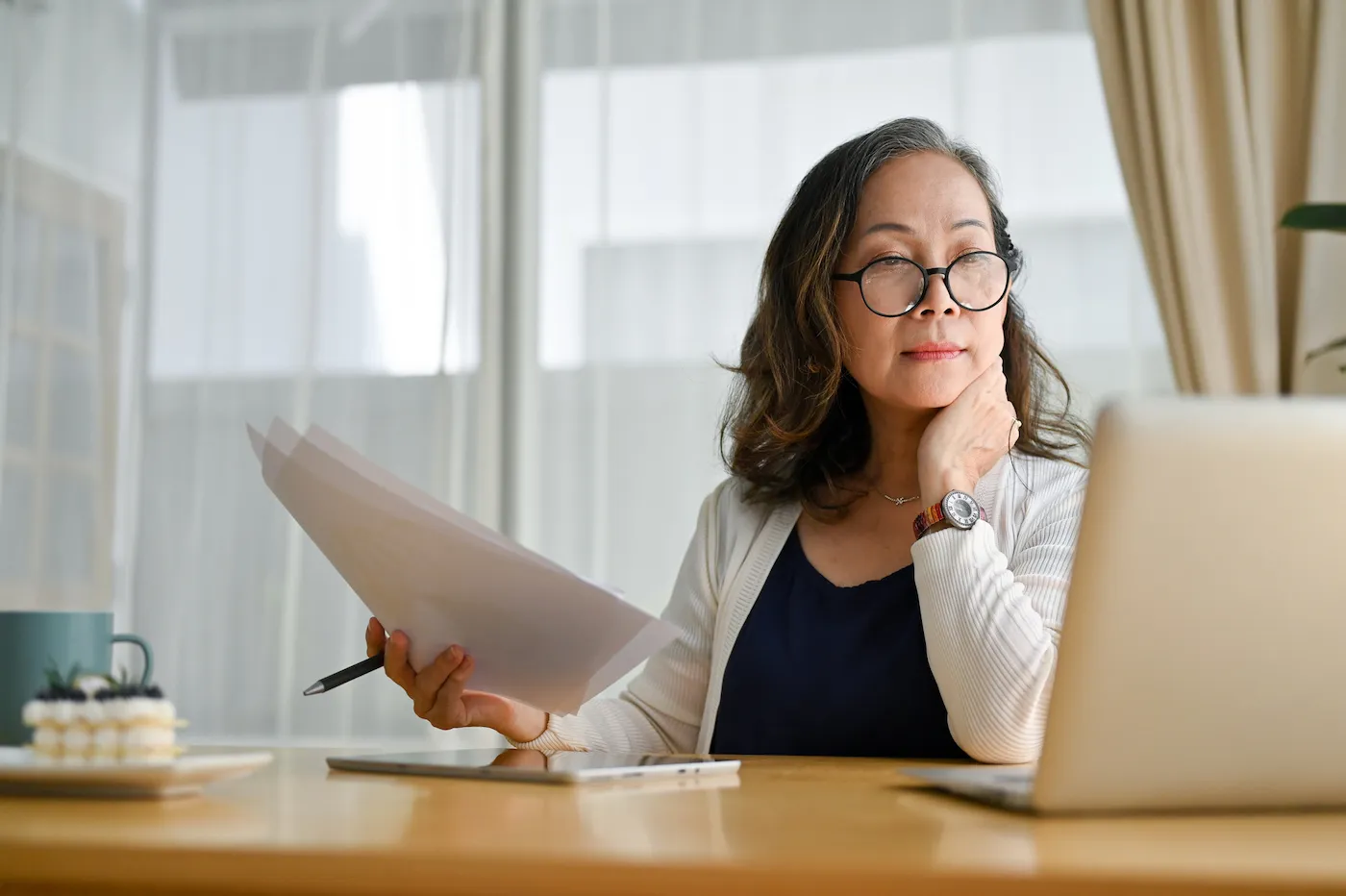 A woman holding papers and looking into an escrow refund on her laptop.