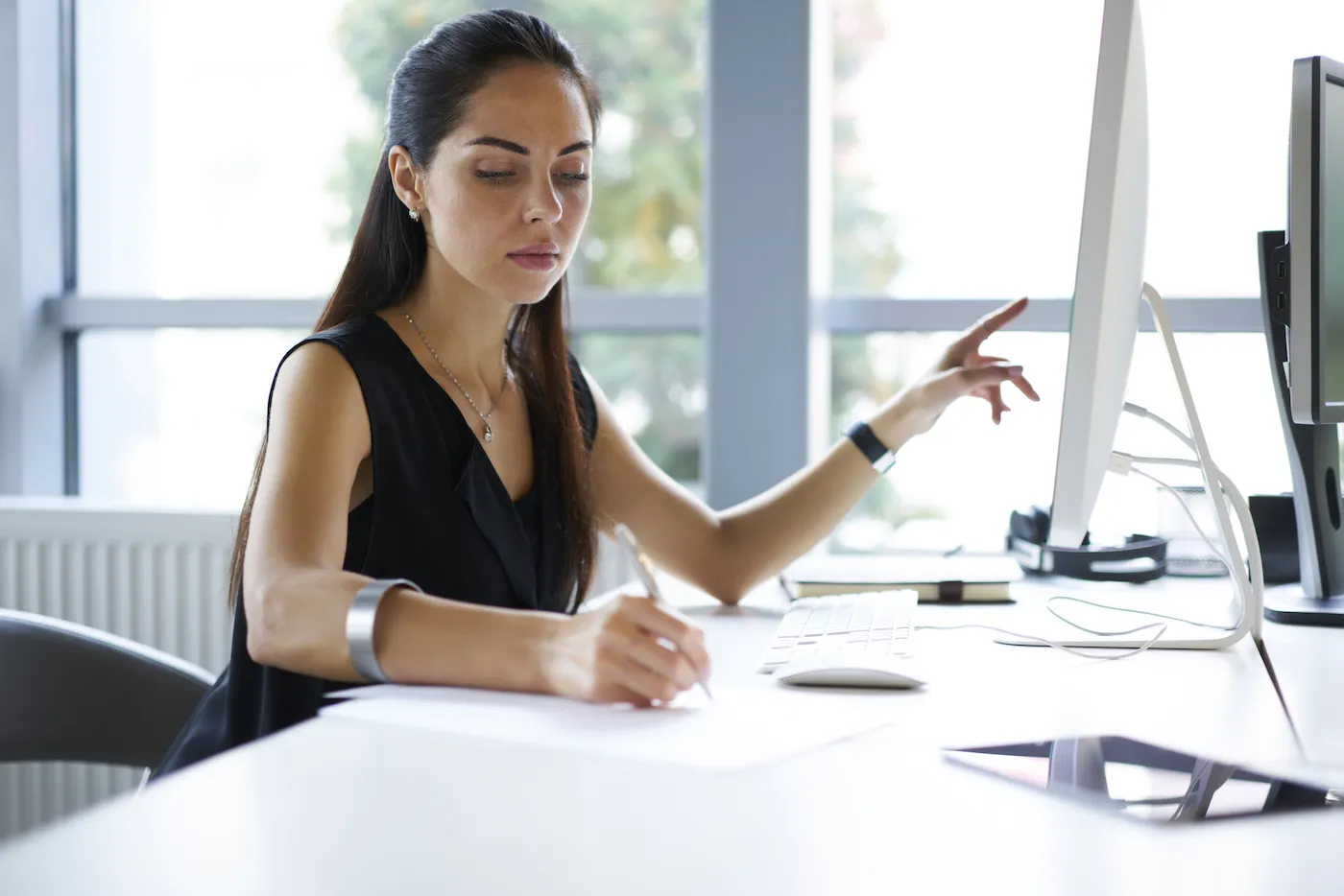 Woman at her desk researching documents on her computer and by hand