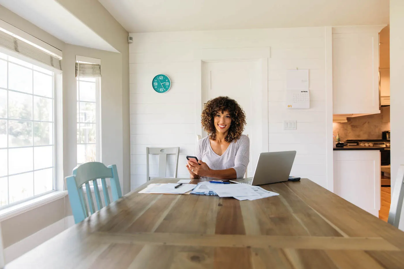 Woman seated at dining room table with laptop and financial reports.