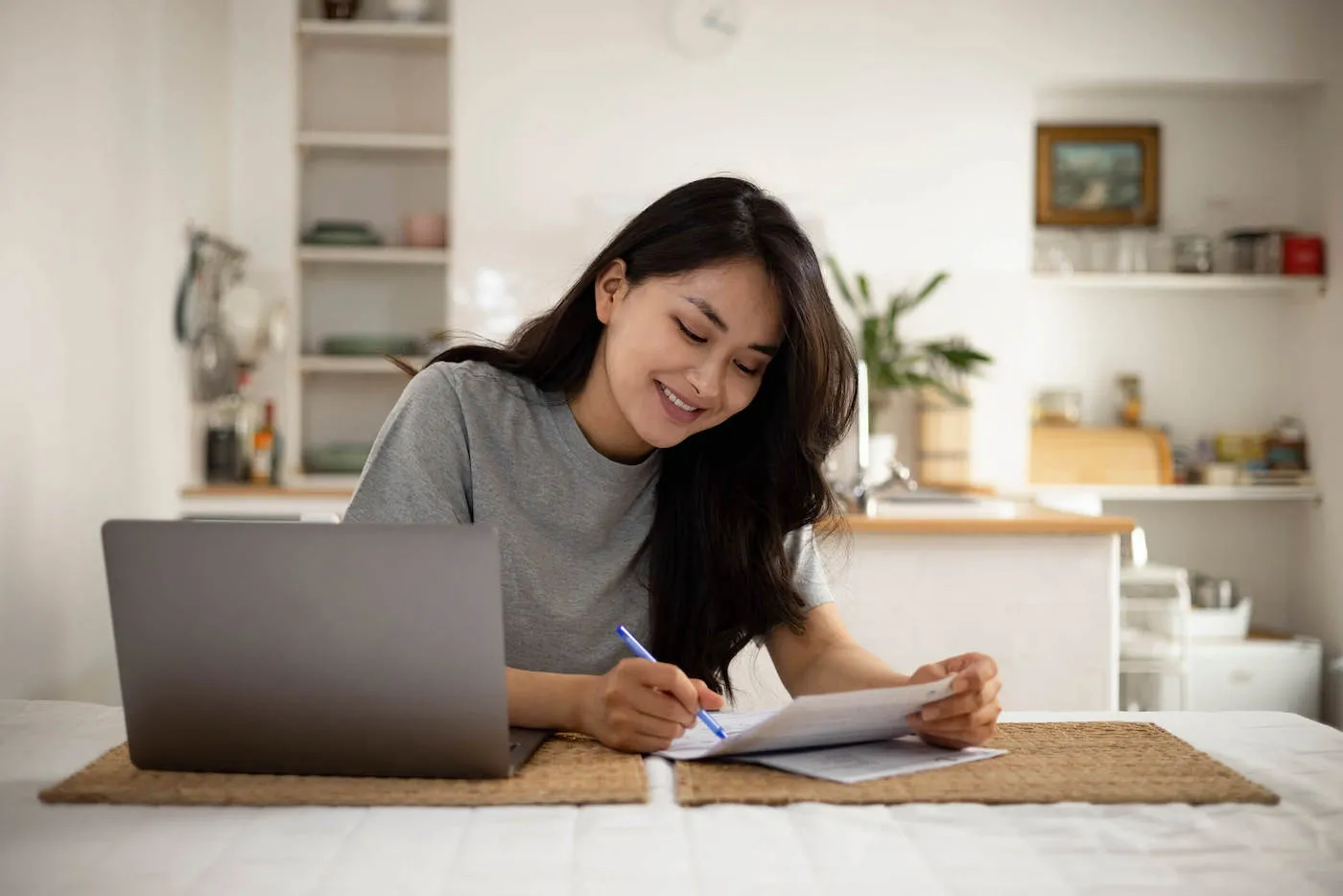 Woman seated by kitchen counter listing house expenses.