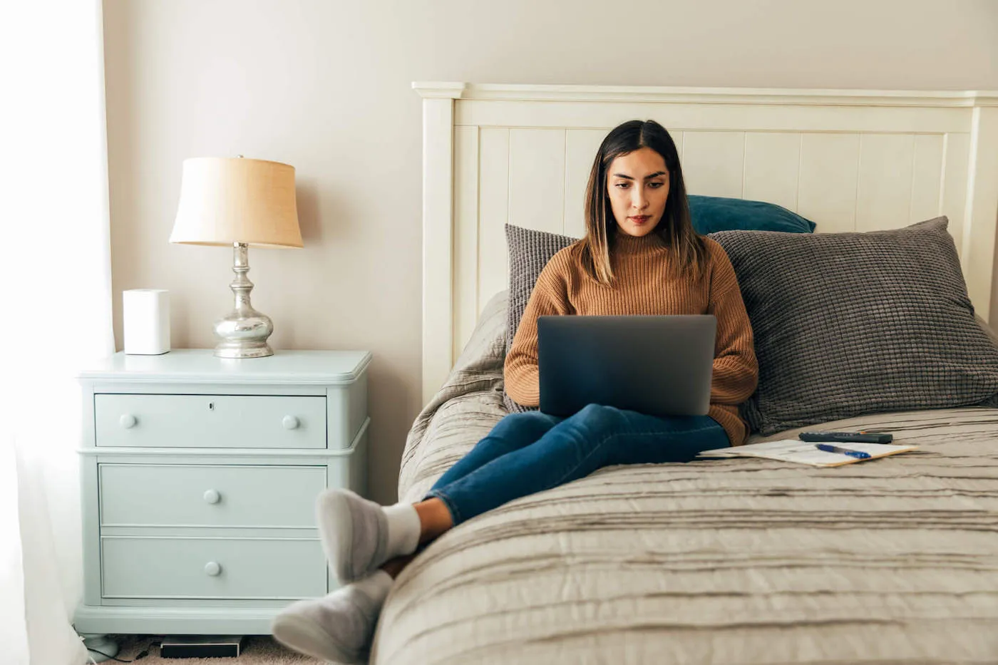 Woman seated on bed paying her rent online.