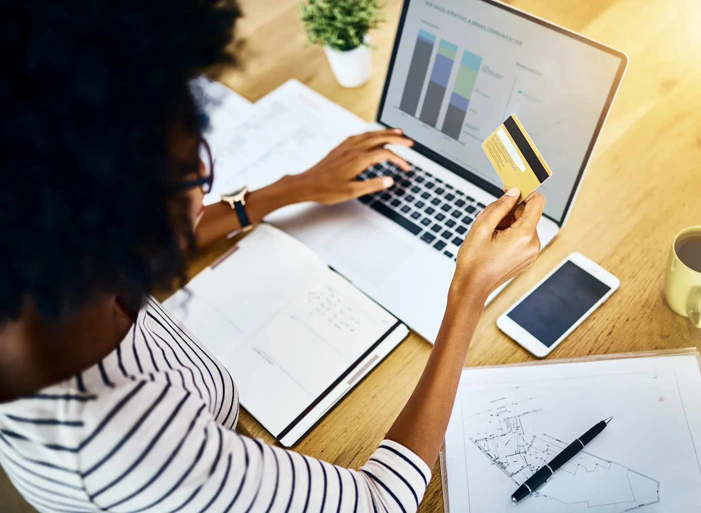 Over the shoulder shot of a woman holding a credit card and setting up automatic payments on her laptop