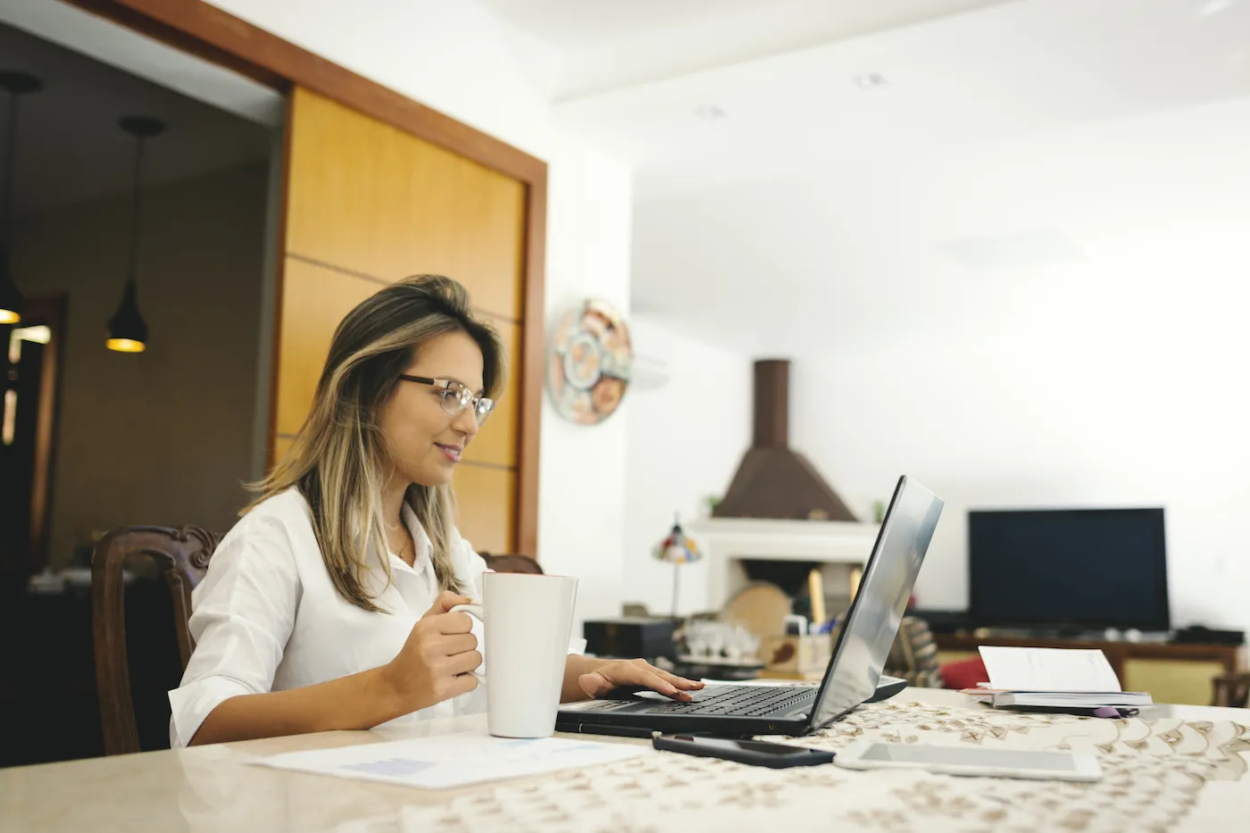 A woman using a laptop to track her spending, sitting at a desk holding a coffee mug.