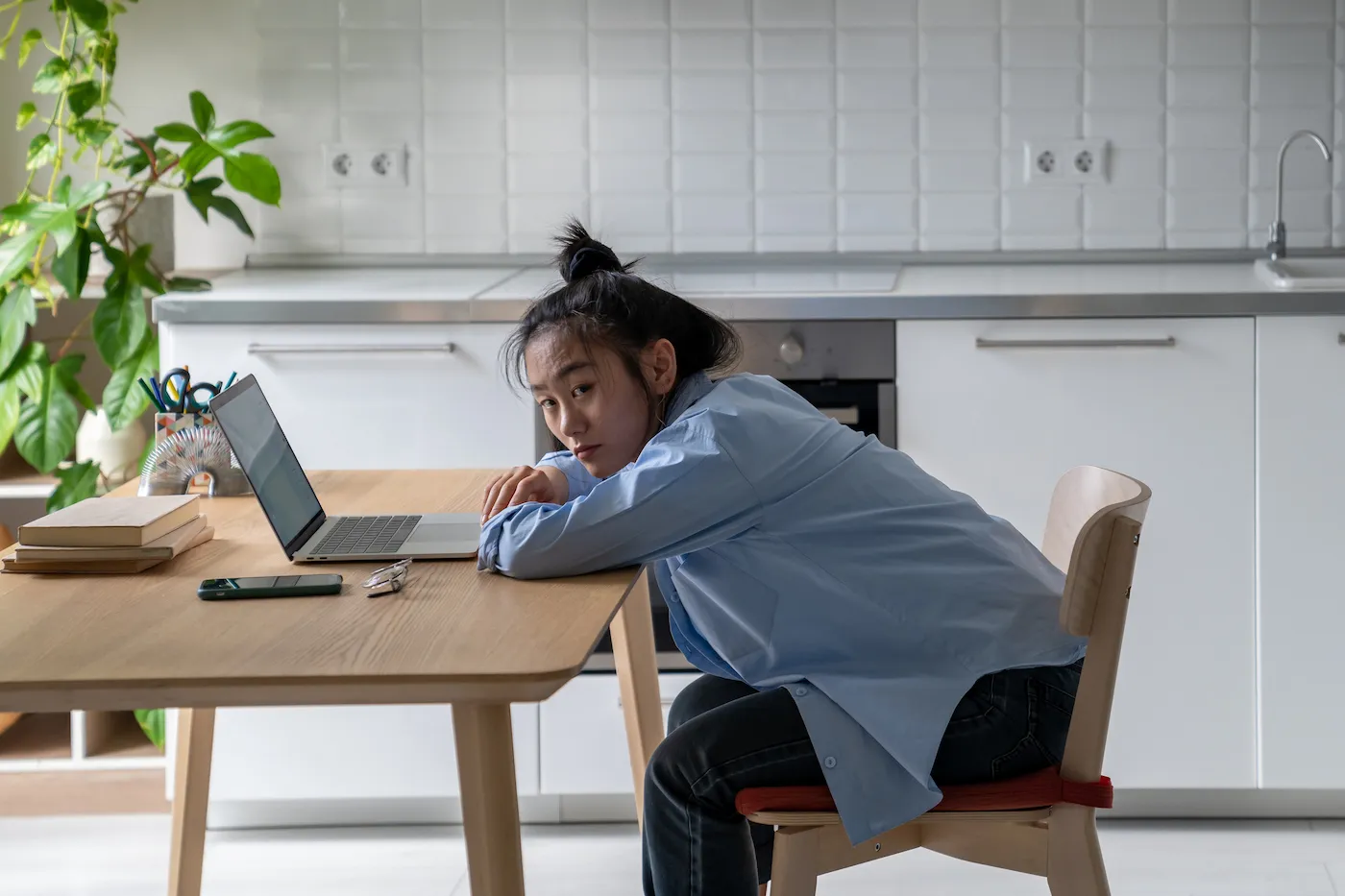 Unhappy woman sitting in front of laptop at kitchen table, stressed about finances.