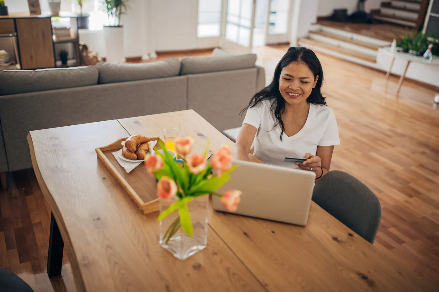 A woman sitting at the dining table at home. She is holding a credit card and using her laptop to check her credit score.