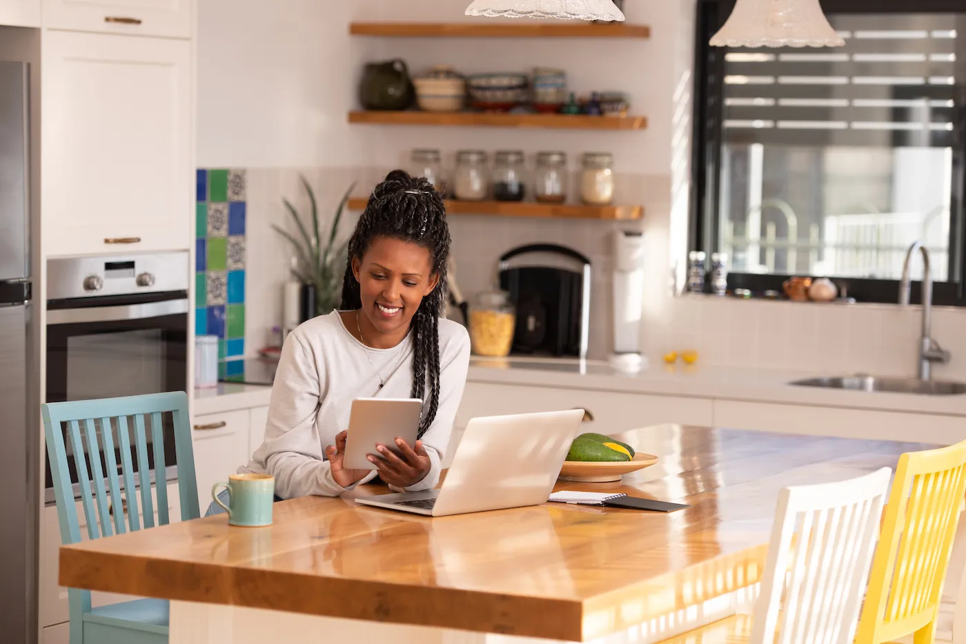 A woman using a tablet PC and laptop to work on her budget while sitting in the kitchen